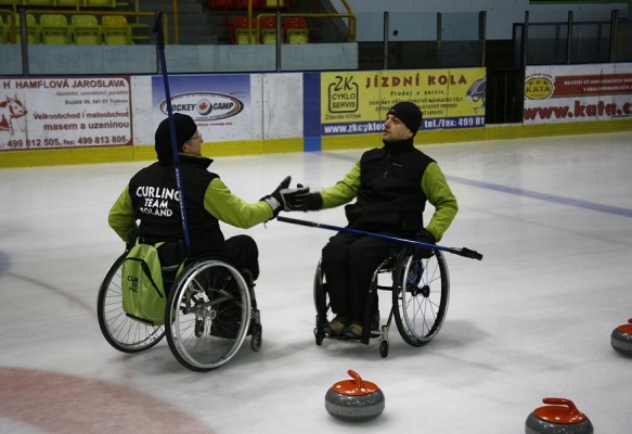Na zdjęciu dwóch zawodników curlingu na wózkach przybija sobie piątkę>