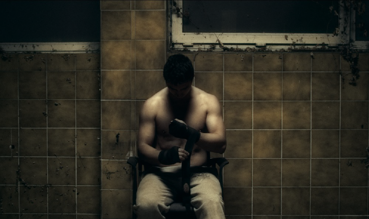 Na grafice kadr z filmu Serce do walki - mężczyzna przygotowujący się do walki owija nadgarstki bandażem.