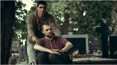 Na grafice kadr z filmu Serce do walki - dwaj mężczyźni, jeden z nich jest na wózku, drugi stoi za nim.