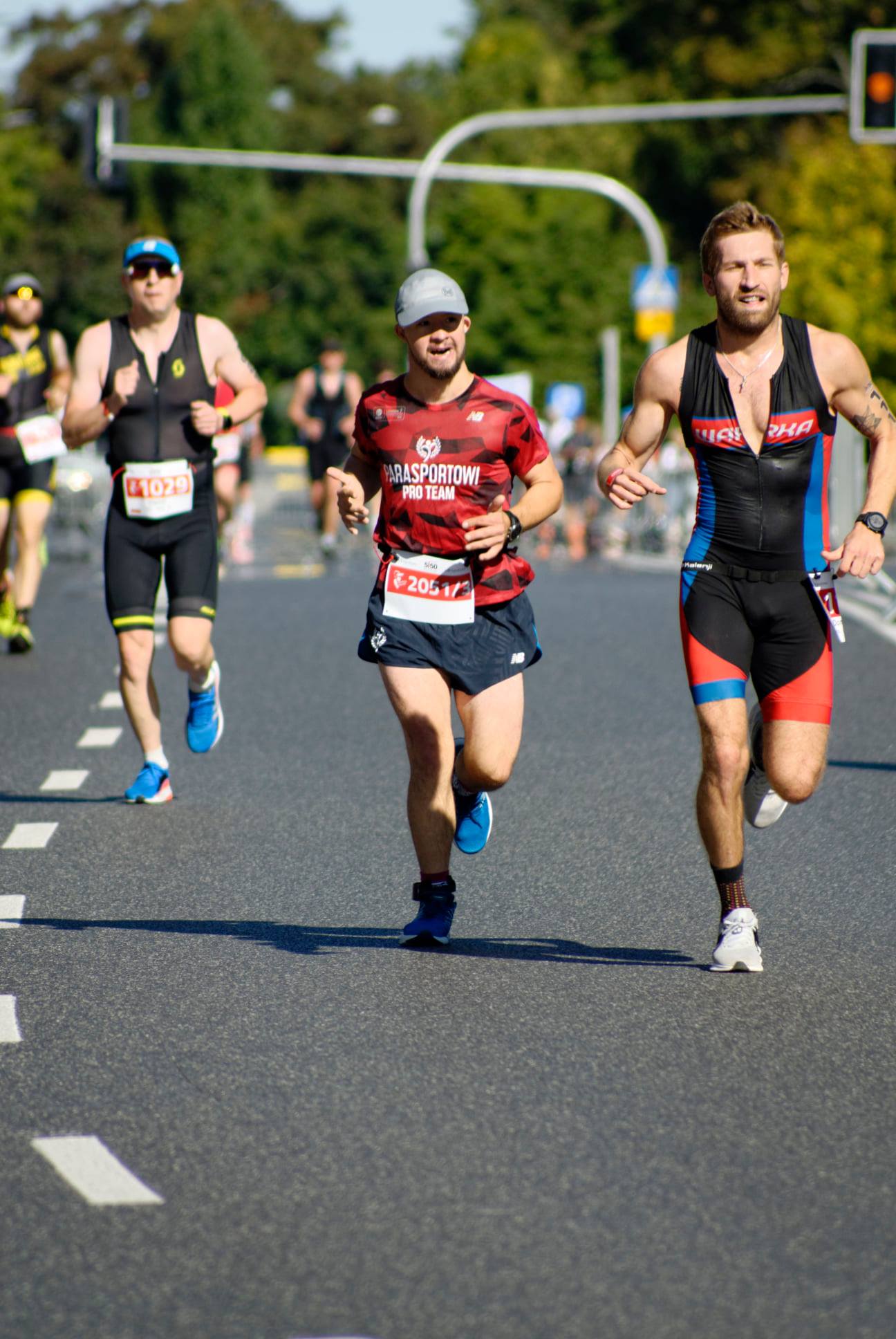 Na zdjęciu znajduje się Filip Walecki, który biegnie wśród innych zawodników na maratonie.