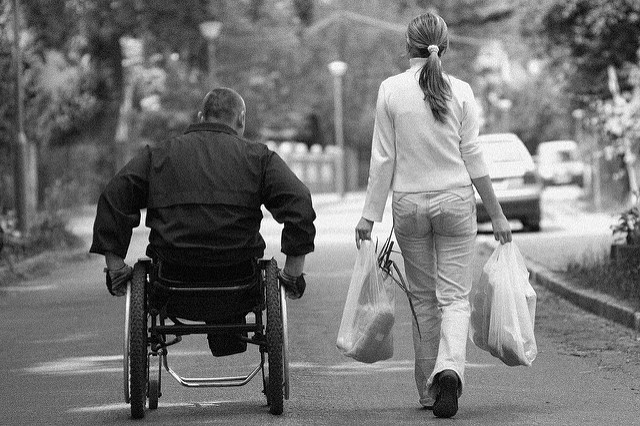 mężczyzna na wózku i kobieta trzymająca zakupy przemieszczają się wspólnie ulicą