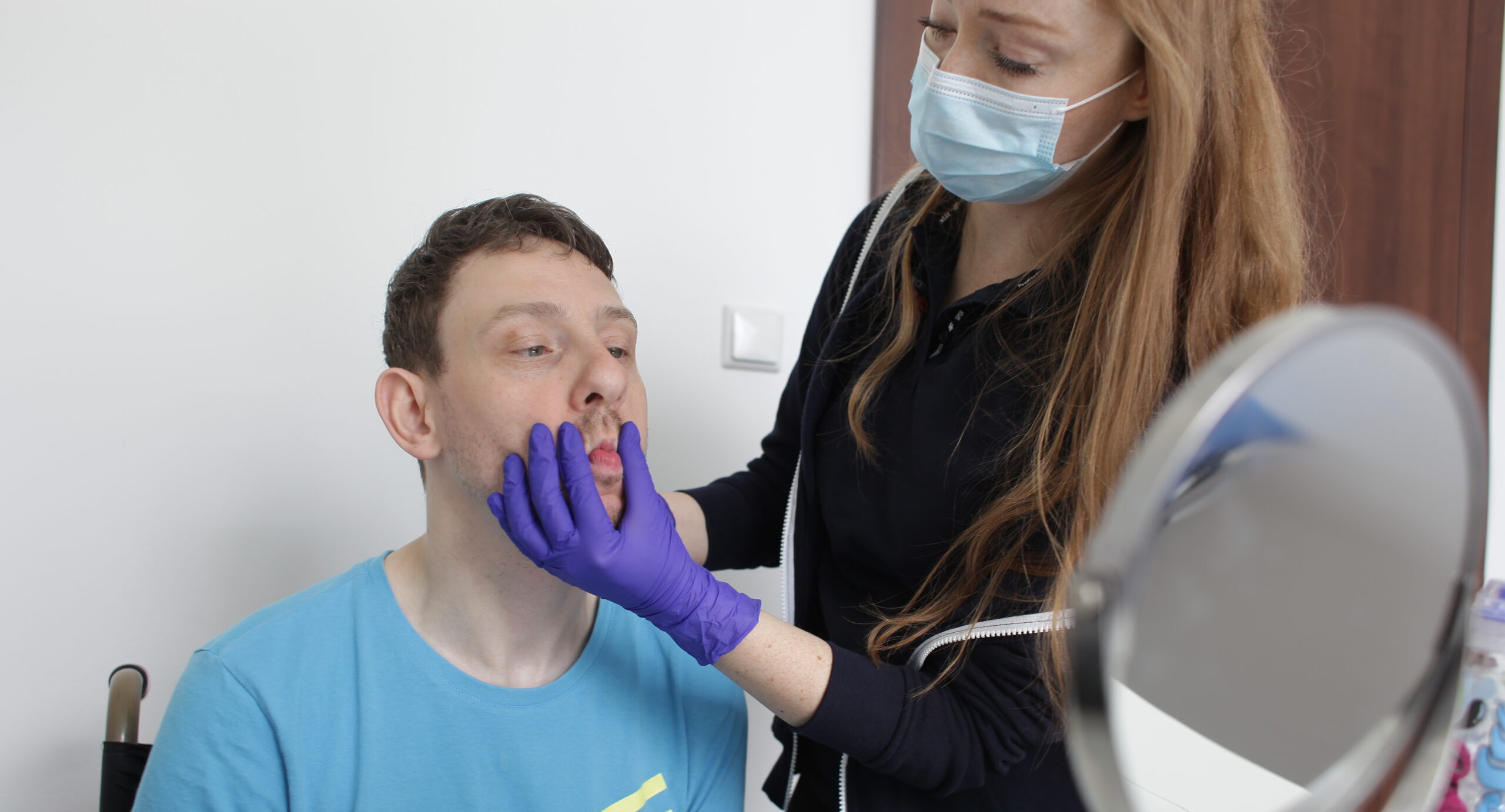 Na zdjęciu logopedka podczas zajęć z pacjentem przy lustrze w trakcie terapii manualnej.