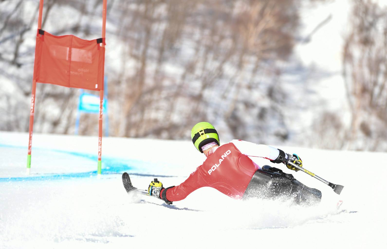 Mężczyzna w stroju reprezentacji Polski, jedzie na mono-ski (specjalnej narcie, na której człowiek porusza się w pozycji siedzącej)