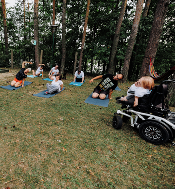 Zdjęcie na którym jest grupa osób z niepełnosprawnościami ćwiczącymi jogę w lesie.