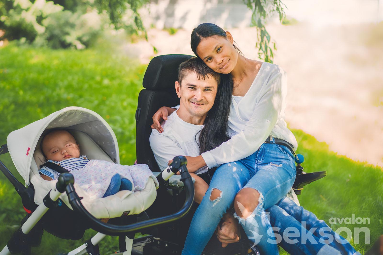 Marebel siedzi na kolanach Adama, są przytuleni. Obok nich soi wózek, w którym śpi Maksymilian.