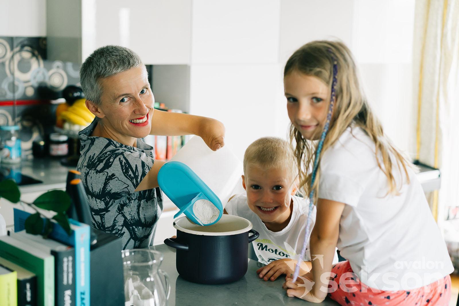 Kasia wsypuję mąkę do garnka, obok niej są jej dzieci Olimpia i Jaś. Wszyscy się uśmiechają.